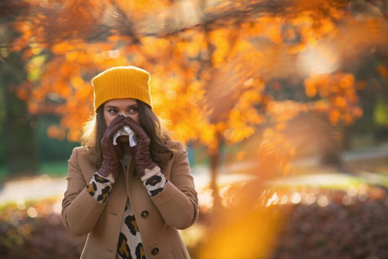 women blowing her nose and sneezing in a park during the fall.