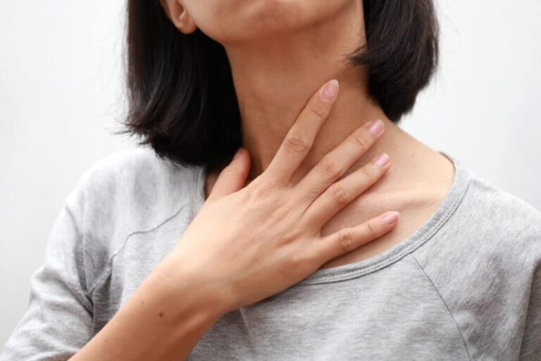 Woman putting her hand up to her sore throat.
