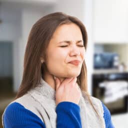 Woman holding her sore throat looking uncomfortable