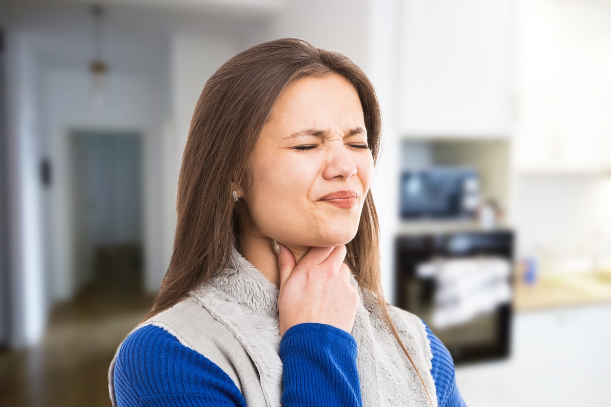Woman holding her sore throat looking uncomfortable.