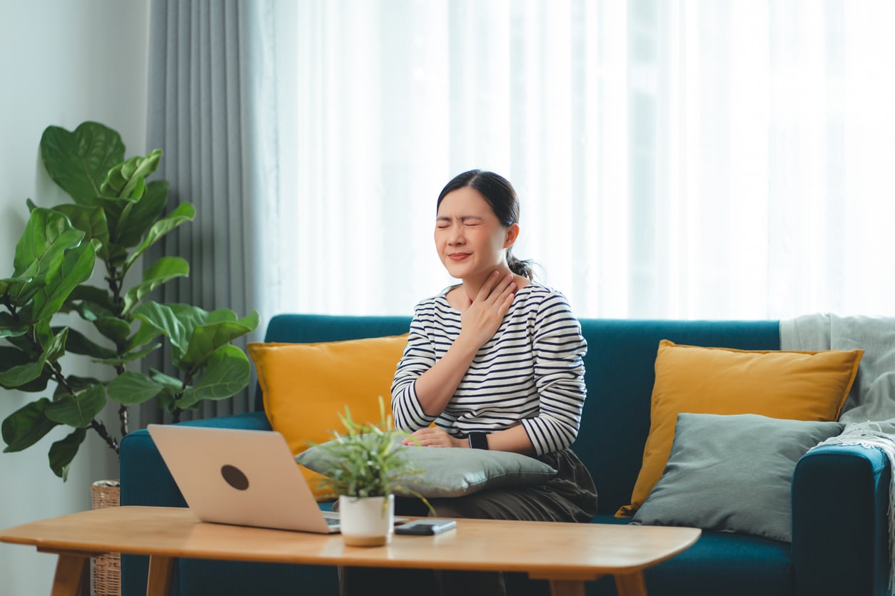 Woman with postnasal drip holding her throat.